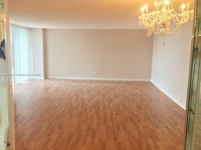 empty room with hardwood / wood-style floors and a notable chandelier