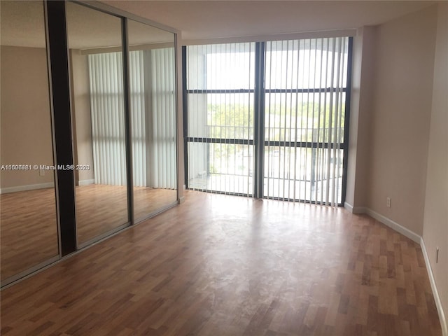 unfurnished bedroom with wood-type flooring, a wall of windows, a closet, and access to exterior