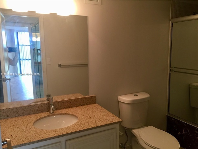 bathroom featuring a shower with door, vanity, and toilet