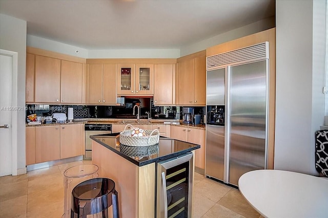 kitchen featuring light brown cabinetry, beverage cooler, tasteful backsplash, a center island, and appliances with stainless steel finishes