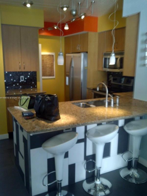 kitchen featuring light stone countertops, decorative light fixtures, a kitchen breakfast bar, appliances with stainless steel finishes, and sink