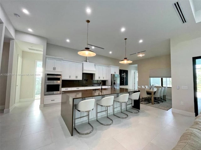 kitchen with appliances with stainless steel finishes, white cabinetry, a center island with sink, and decorative light fixtures