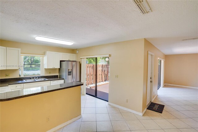 kitchen featuring stainless steel fridge, light tile patterned floors, a healthy amount of sunlight, and white cabinets