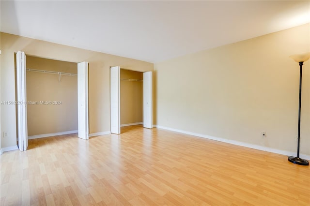 unfurnished bedroom featuring multiple closets and light hardwood / wood-style floors