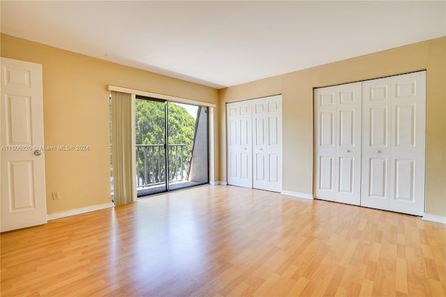 unfurnished bedroom with access to exterior, light hardwood / wood-style flooring, and two closets