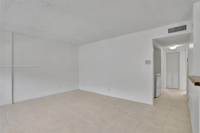 spare room featuring washer / dryer, light tile flooring, and a textured ceiling