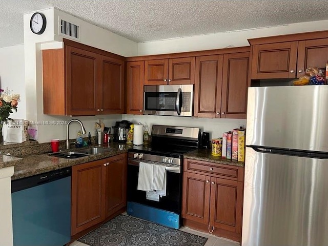 kitchen featuring dark stone counters, stainless steel appliances, tile flooring, sink, and a textured ceiling