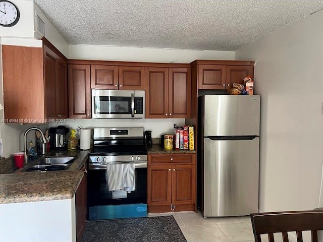 kitchen with a textured ceiling, dark stone countertops, stainless steel appliances, sink, and light tile floors