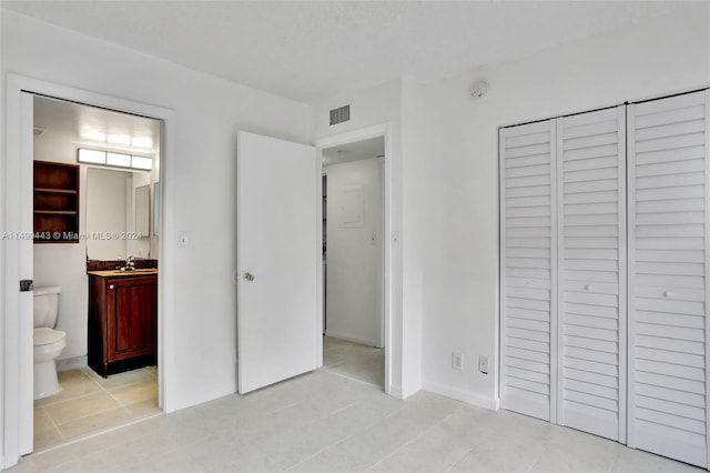 unfurnished bedroom featuring ensuite bathroom, a closet, and light tile flooring