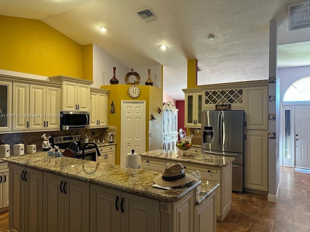 kitchen with appliances with stainless steel finishes, decorative backsplash, light stone counters, cream cabinetry, and a kitchen island