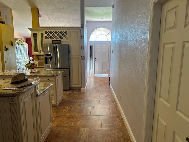 kitchen with stainless steel refrigerator with ice dispenser, tile patterned flooring, light stone counters, a textured ceiling, and a kitchen island