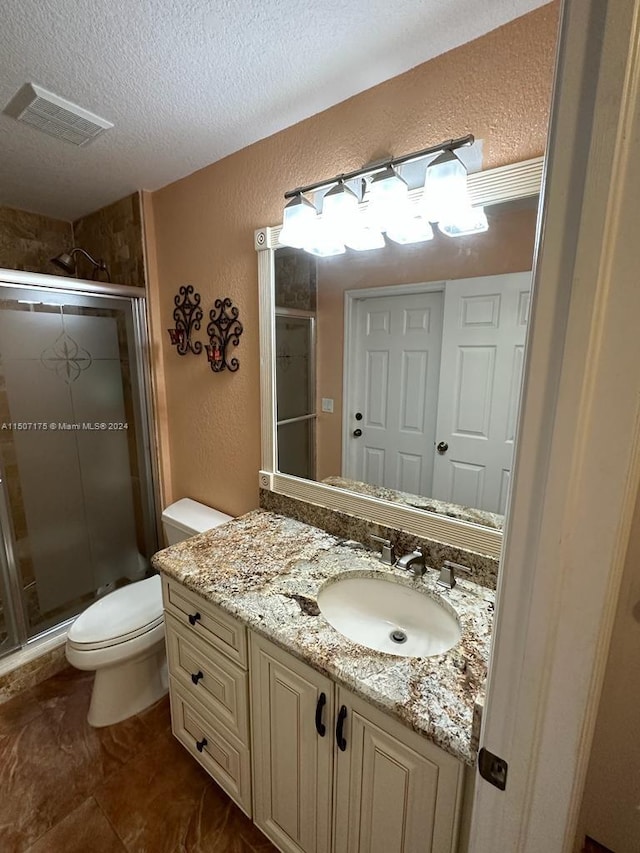 bathroom with vanity, tile patterned floors, a textured ceiling, toilet, and a shower with door