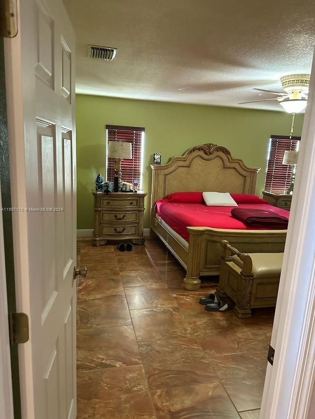 bedroom featuring ceiling fan, dark tile patterned floors, multiple windows, and a textured ceiling