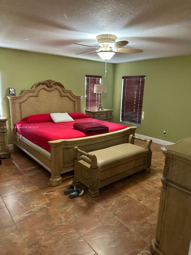 bedroom with ceiling fan, dark tile patterned floors, and a textured ceiling