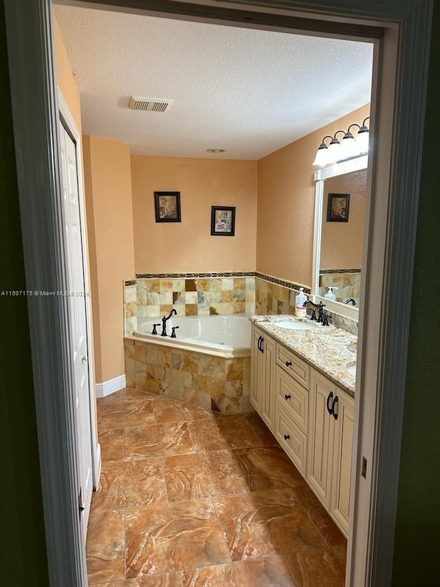 bathroom with a textured ceiling, a relaxing tiled tub, tile patterned flooring, and dual bowl vanity