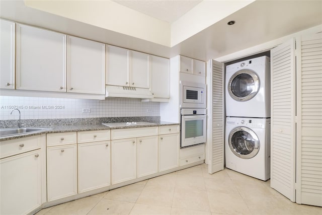 kitchen with a sink, white appliances, light tile patterned floors, under cabinet range hood, and stacked washer and clothes dryer
