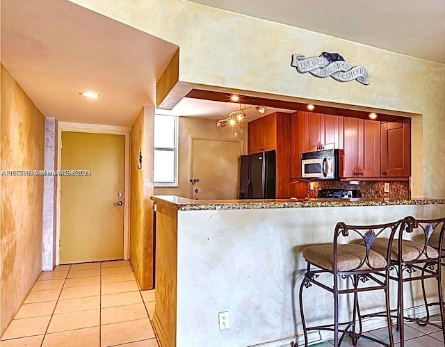 kitchen with light tile patterned flooring, stone countertops, kitchen peninsula, and black fridge