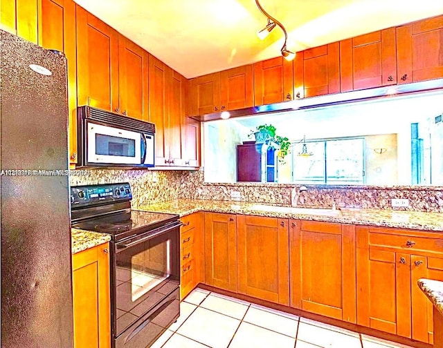 kitchen featuring sink, black appliances, light stone countertops, light tile patterned floors, and track lighting