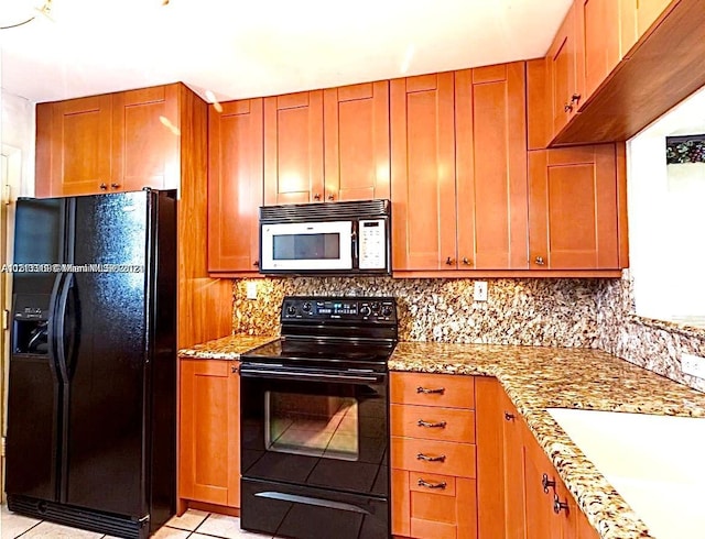 kitchen with light tile patterned flooring, backsplash, light stone counters, and black appliances