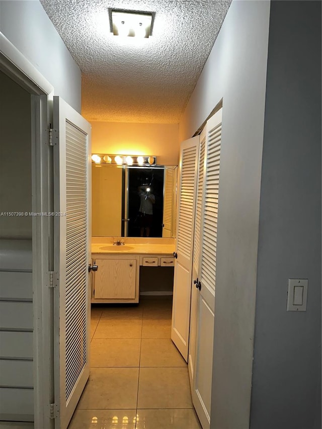 corridor featuring a textured ceiling, light tile patterned flooring, and sink