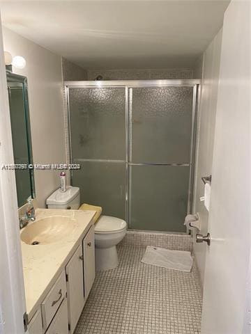 bathroom with tile patterned floors, vanity, a shower with shower door, and toilet