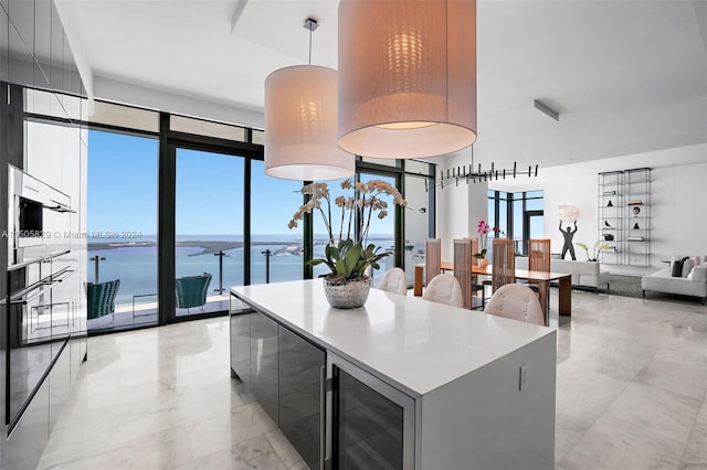 kitchen with decorative light fixtures, light tile flooring, a water view, beverage cooler, and a kitchen island