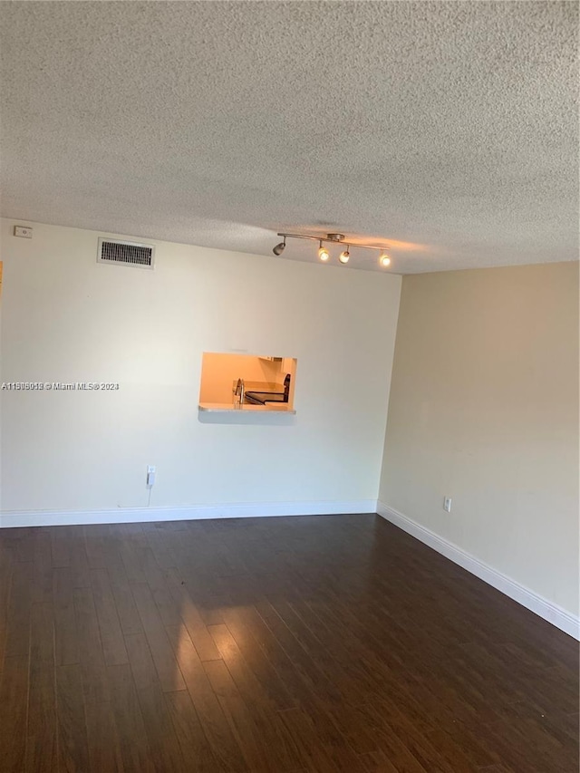 unfurnished room featuring dark hardwood / wood-style floors, a textured ceiling, and track lighting