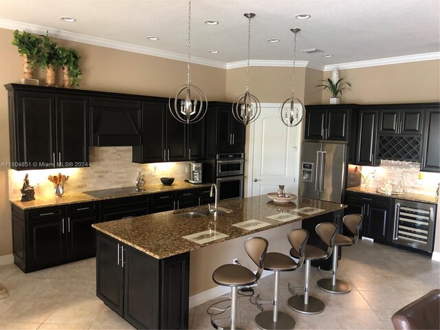 kitchen featuring custom exhaust hood, stainless steel appliances, sink, hanging light fixtures, and an island with sink