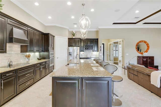 kitchen with a kitchen bar, premium range hood, sink, pendant lighting, and an island with sink