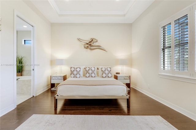 bedroom with ensuite bathroom, ornamental molding, dark wood-type flooring, and a tray ceiling