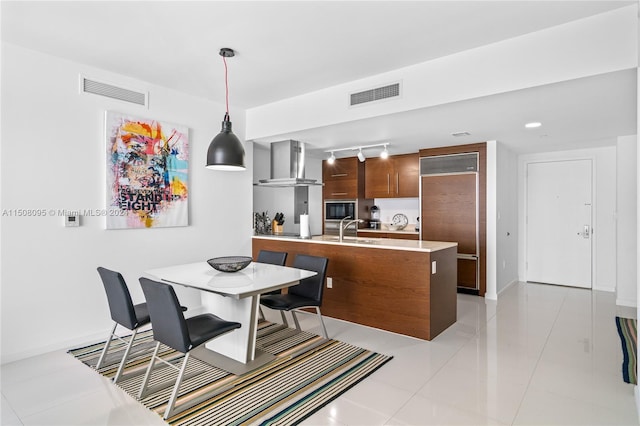 kitchen with pendant lighting, light tile floors, built in microwave, track lighting, and wall chimney exhaust hood