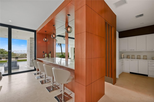 kitchen featuring a wall of windows, hanging light fixtures, kitchen peninsula, a breakfast bar, and white cabinets