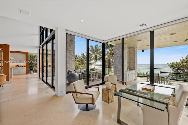 sitting room with plenty of natural light, a water view, and a wall of windows