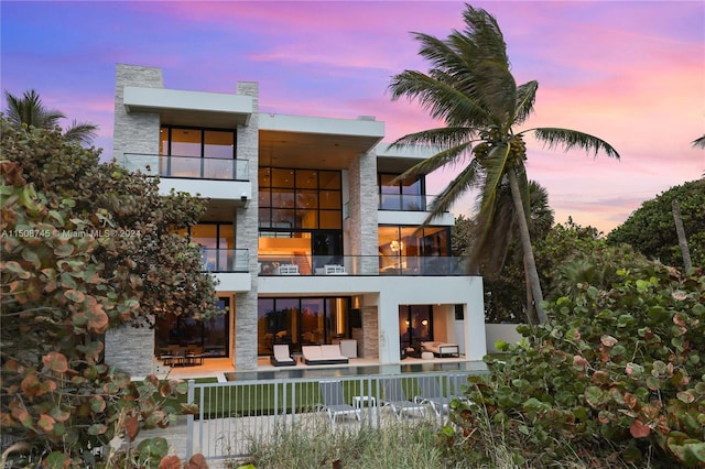 back house at dusk featuring outdoor lounge area, a patio area, and a balcony