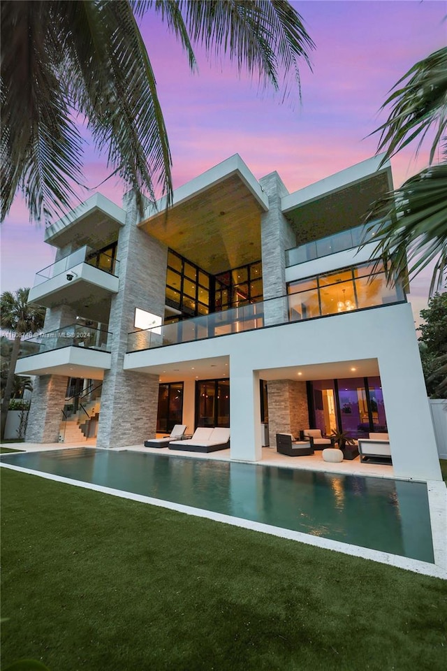 back house at dusk featuring a lawn, a patio, and a balcony