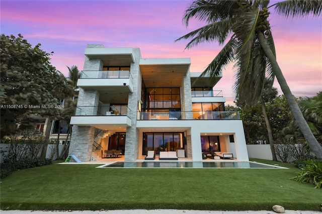 back house at dusk featuring a balcony, a yard, and a patio