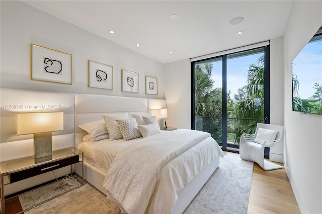 bedroom featuring light wood-type flooring, multiple windows, access to exterior, and a wall of windows