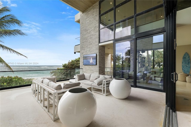 exterior space with a balcony, an outdoor living space, a water view, and a view of the beach