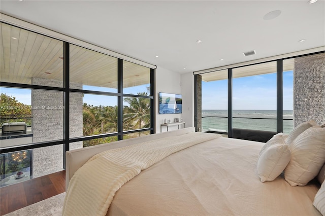 bedroom featuring multiple windows, a water view, hardwood / wood-style flooring, and floor to ceiling windows