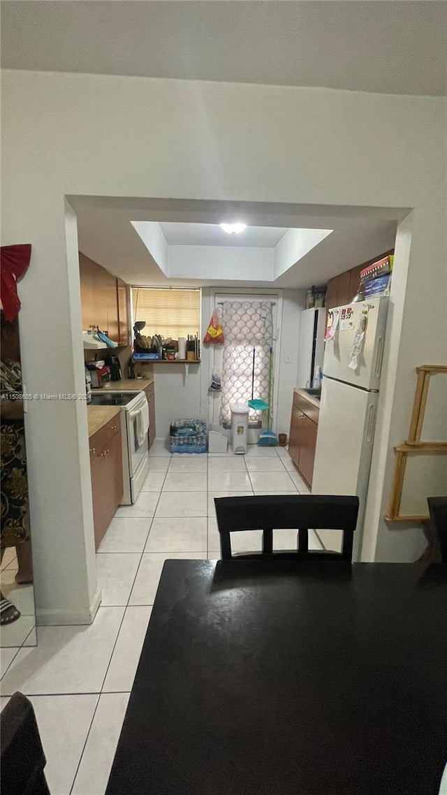 kitchen with a tray ceiling, light tile patterned floors, and white appliances