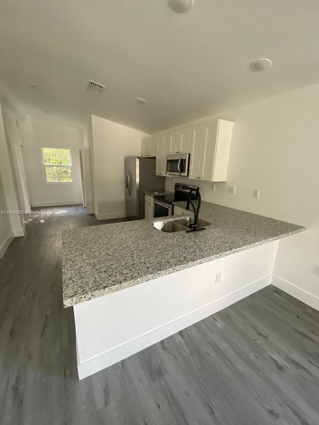 kitchen featuring kitchen peninsula, stainless steel appliances, dark hardwood / wood-style floors, light stone counters, and white cabinets