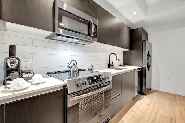 kitchen featuring backsplash, light wood-type flooring, stainless steel appliances, sink, and dark brown cabinets