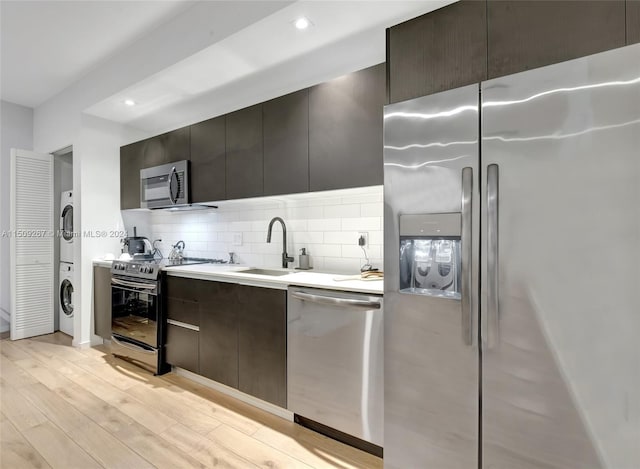 kitchen with light wood-type flooring, appliances with stainless steel finishes, stacked washer and clothes dryer, sink, and decorative backsplash