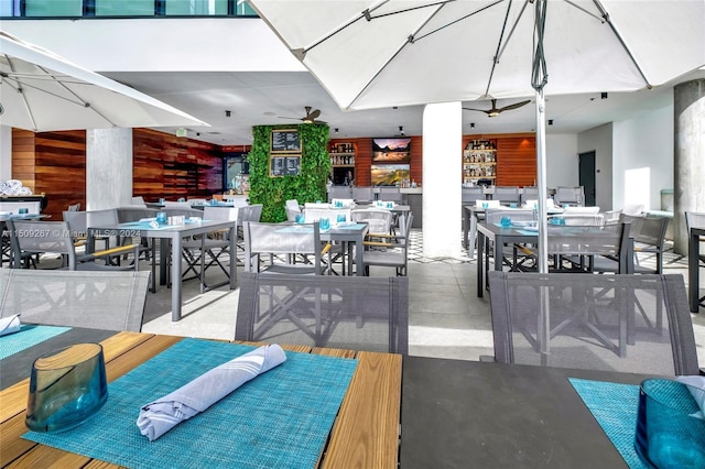 dining area featuring wood walls, ceiling fan, and concrete flooring