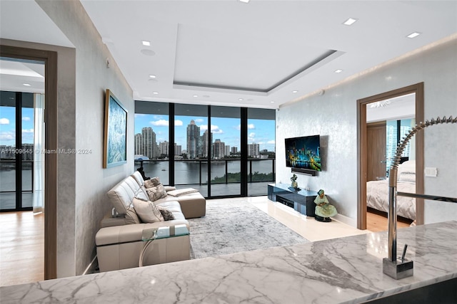 living room with a water view, a tray ceiling, light wood-type flooring, and a wall of windows