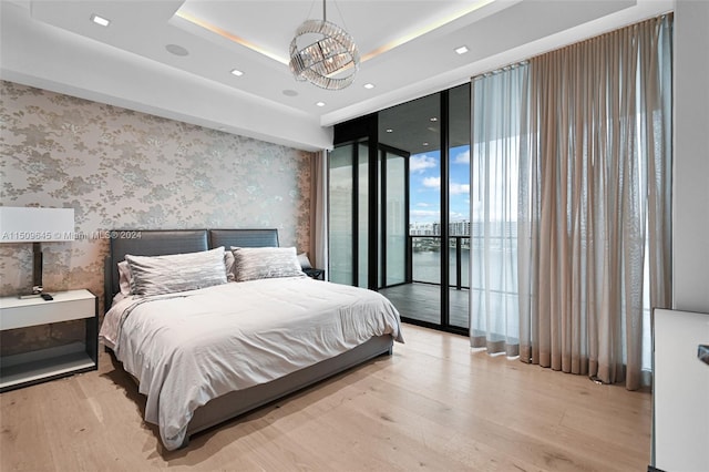 bedroom featuring access to outside, light hardwood / wood-style flooring, expansive windows, and a raised ceiling