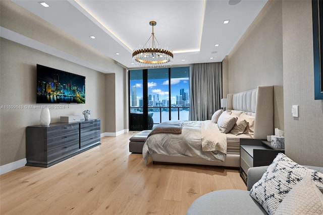 bedroom with light hardwood / wood-style flooring, access to outside, expansive windows, a chandelier, and a raised ceiling