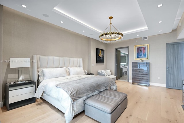 bedroom featuring a chandelier, a raised ceiling, and light hardwood / wood-style flooring