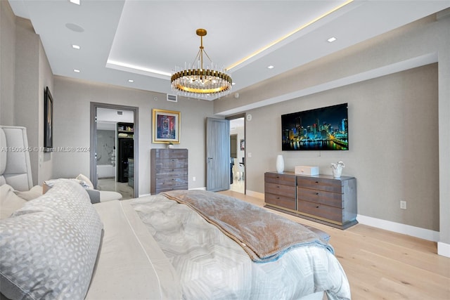 bedroom with a raised ceiling, light wood-type flooring, and a chandelier