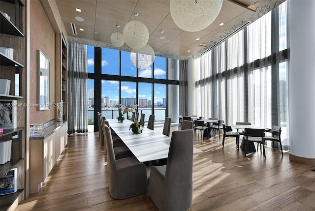 dining area featuring floor to ceiling windows, a towering ceiling, hardwood / wood-style flooring, and a water view